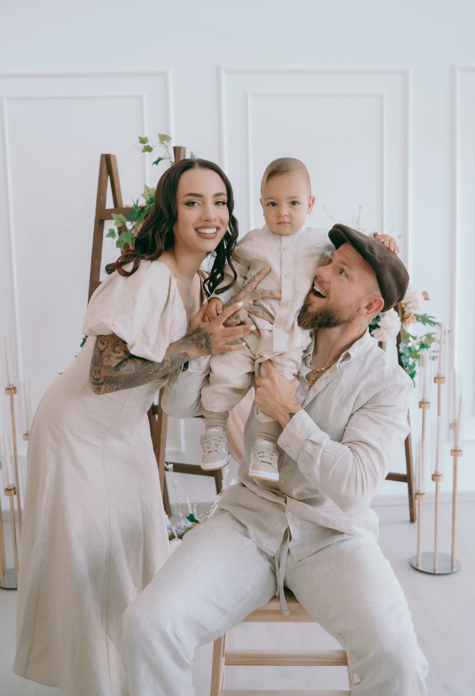 Jonny and Naomi Crawford holding their son Theodoros between them, all dressed in pale linen.